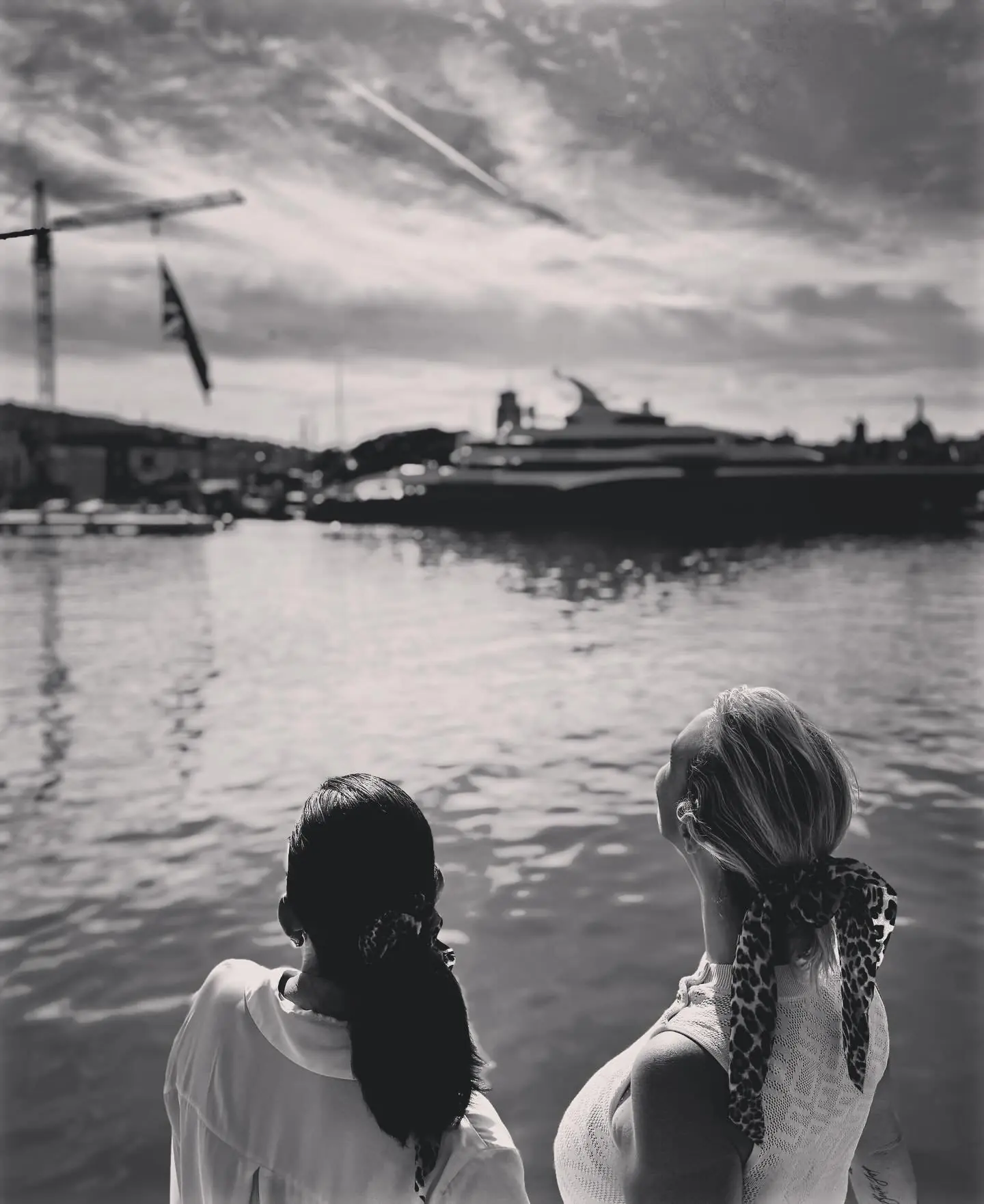 Dos mujeres de espaldas miran el mar desde el puerto, en blanco y negro